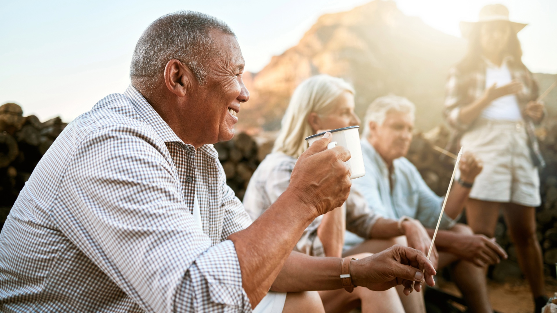 Older friends enjoying coffee together around a campfire outdoors