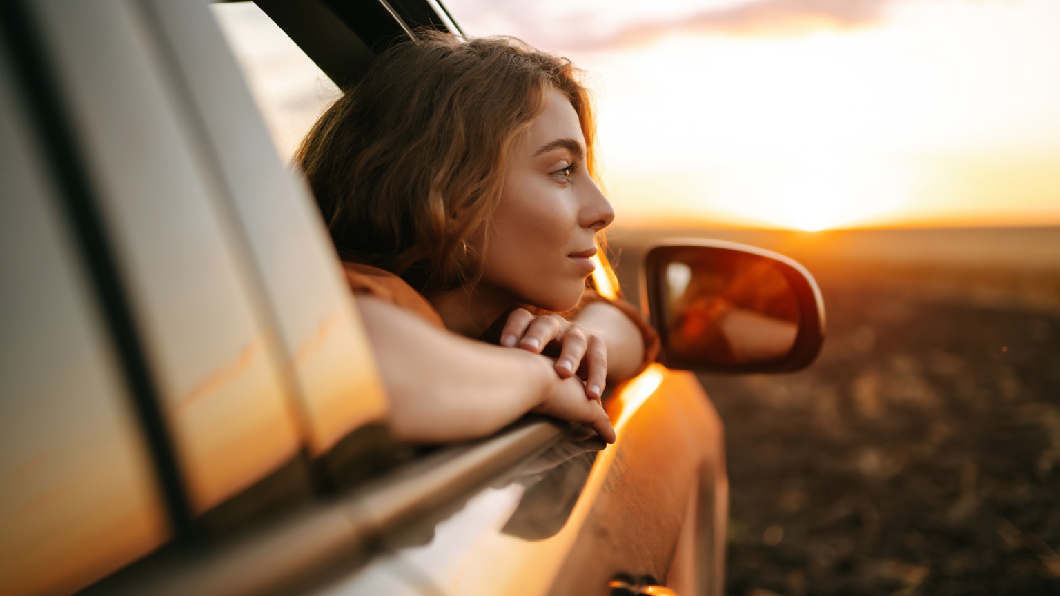 Driver looking out of a car window at sunset