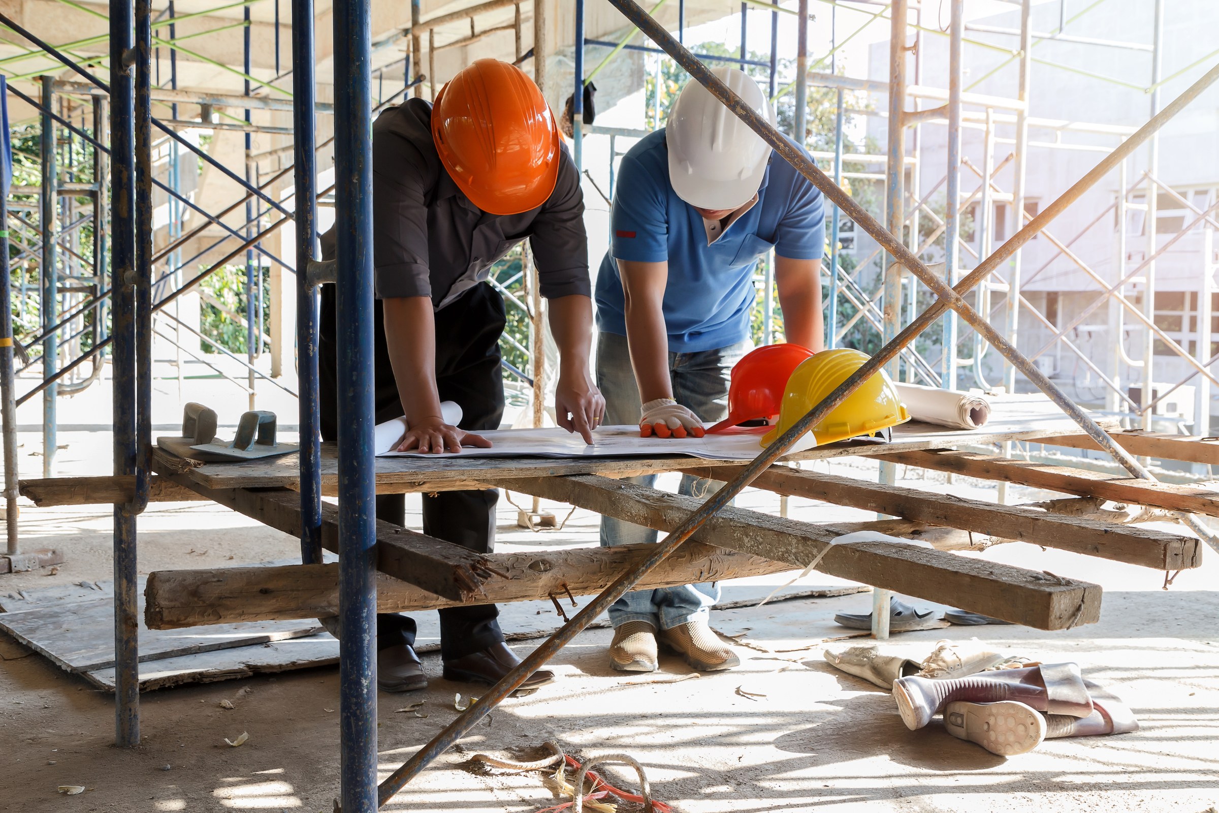 Two construction professionals in hard hats review plans at a building site.