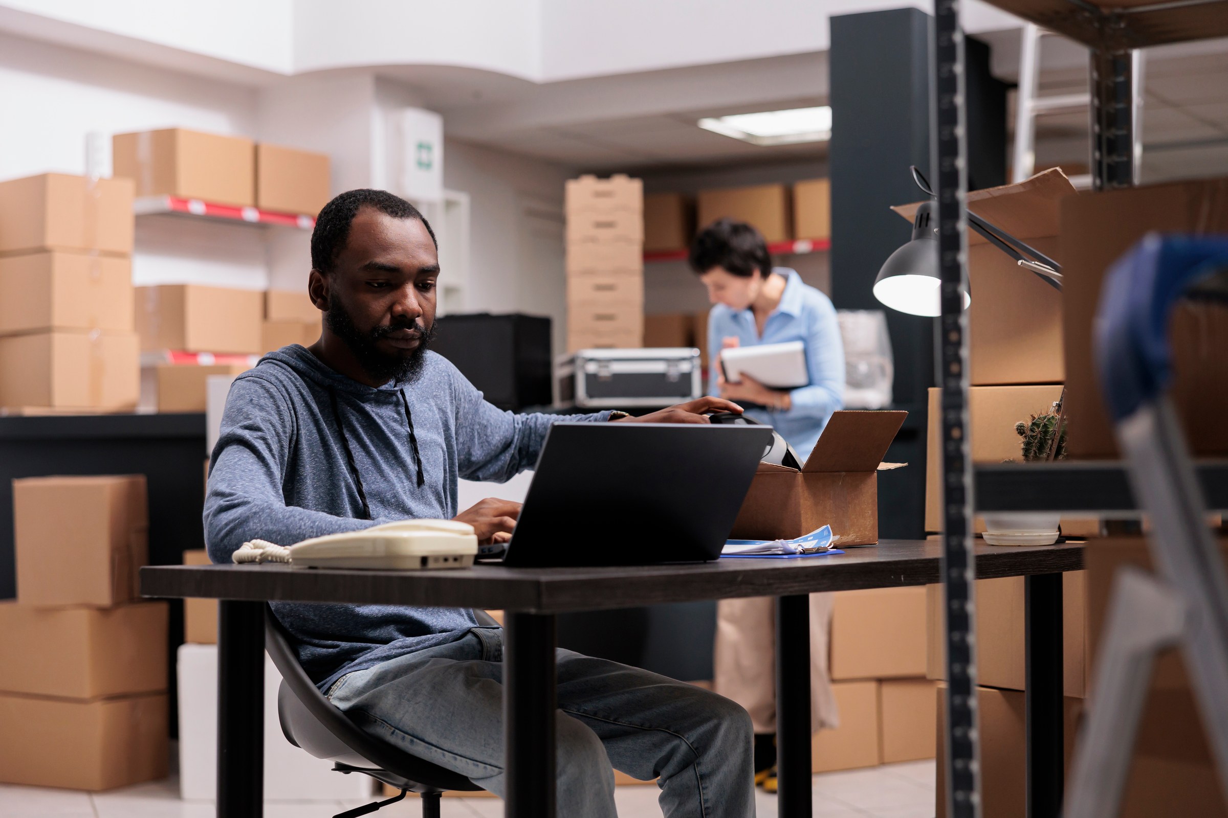 Logistics professional uses a laptop at a desk in a shipping warehouse.