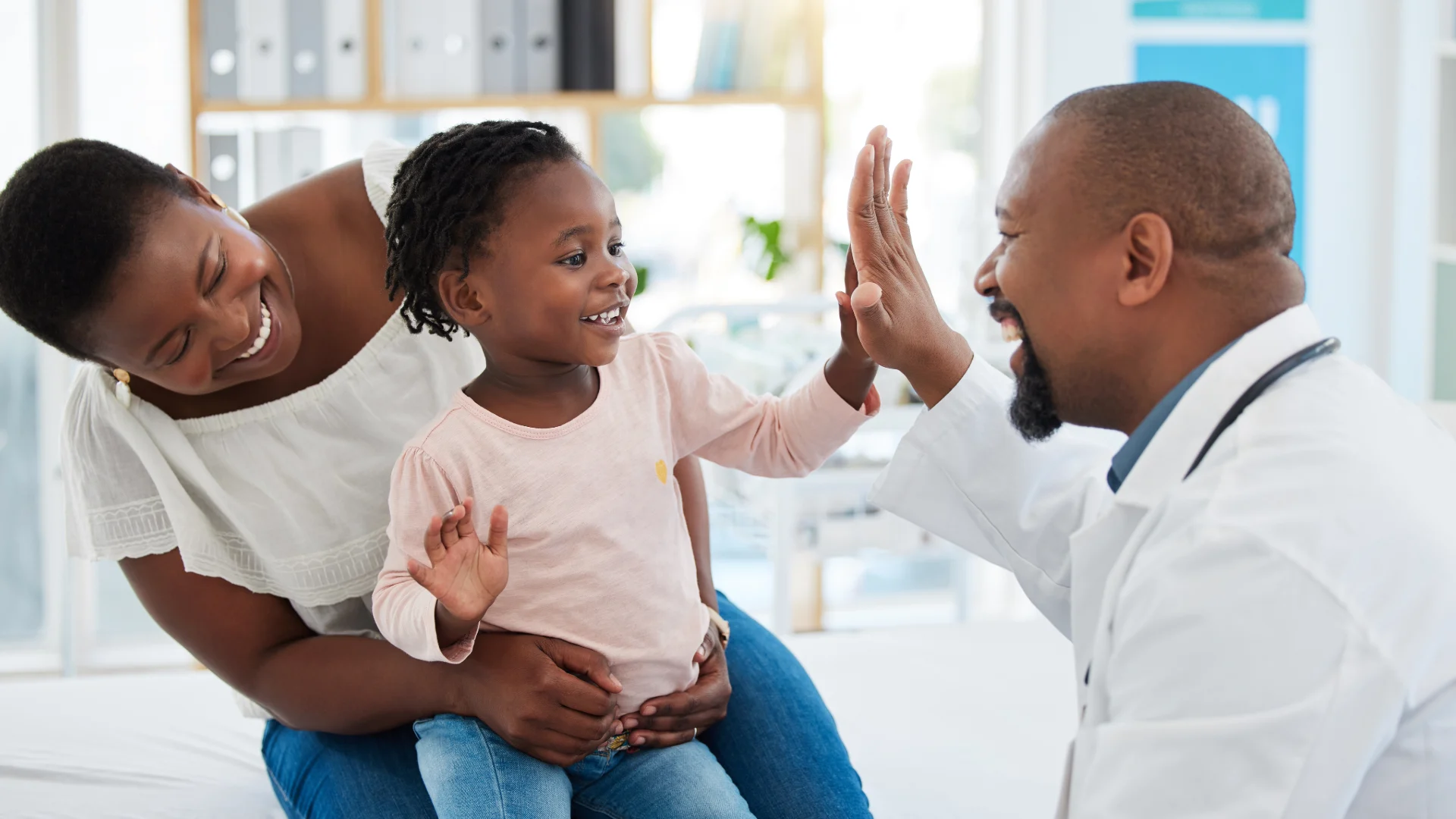 Young child high-fiving a pediatrician while sitting with her mother