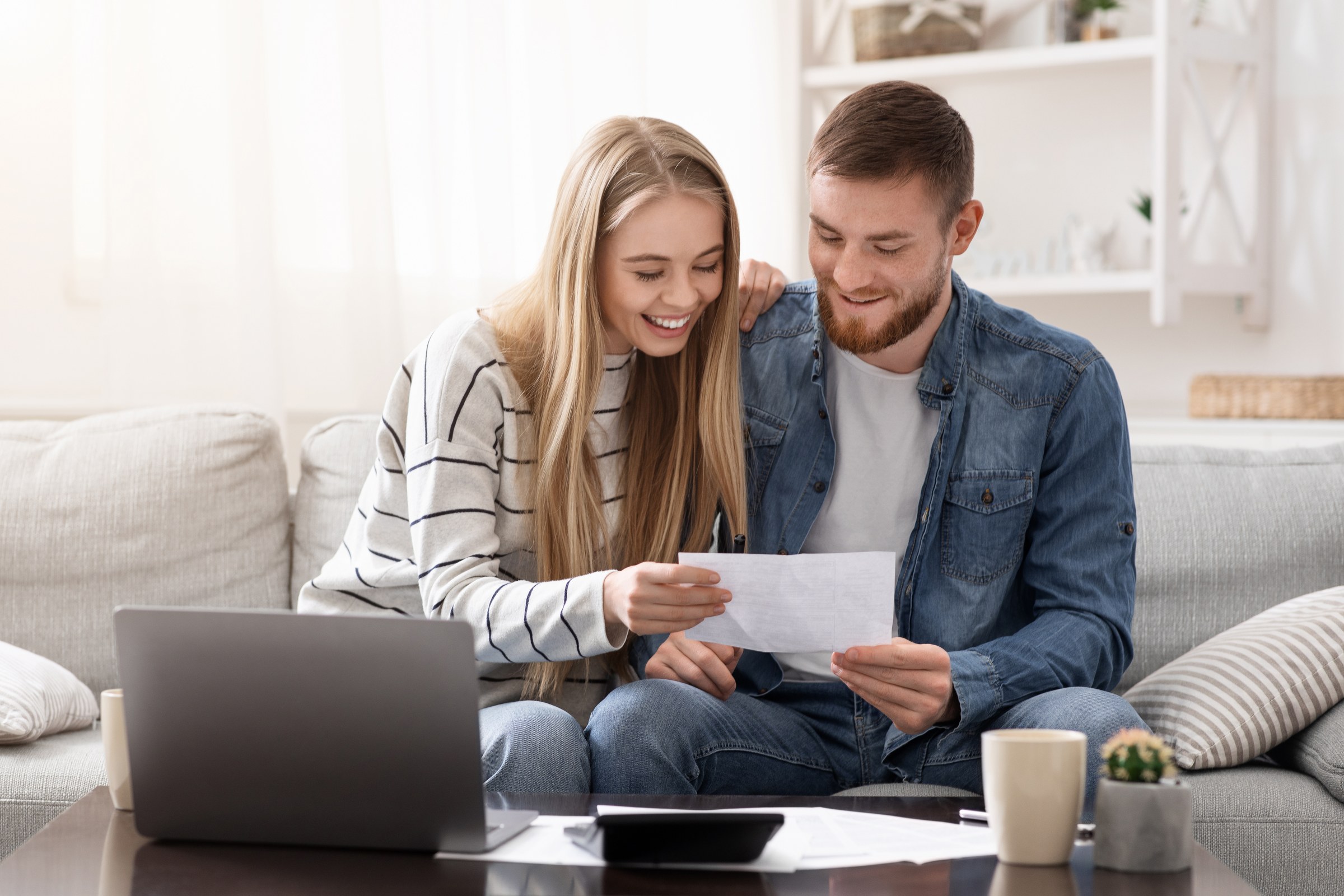 Couple reviewing household paperwork beside a laptop at home.