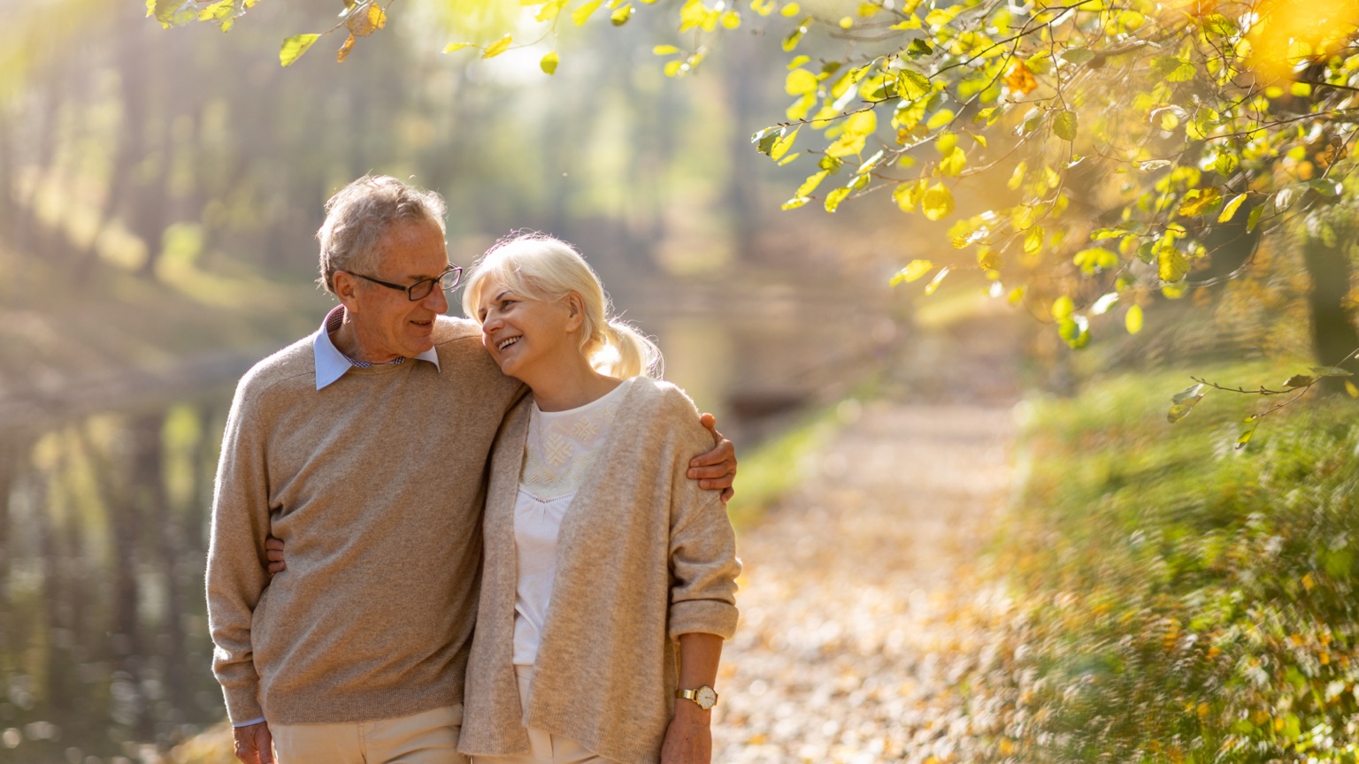 Older couple walking together outdoors beneath autumn leaves