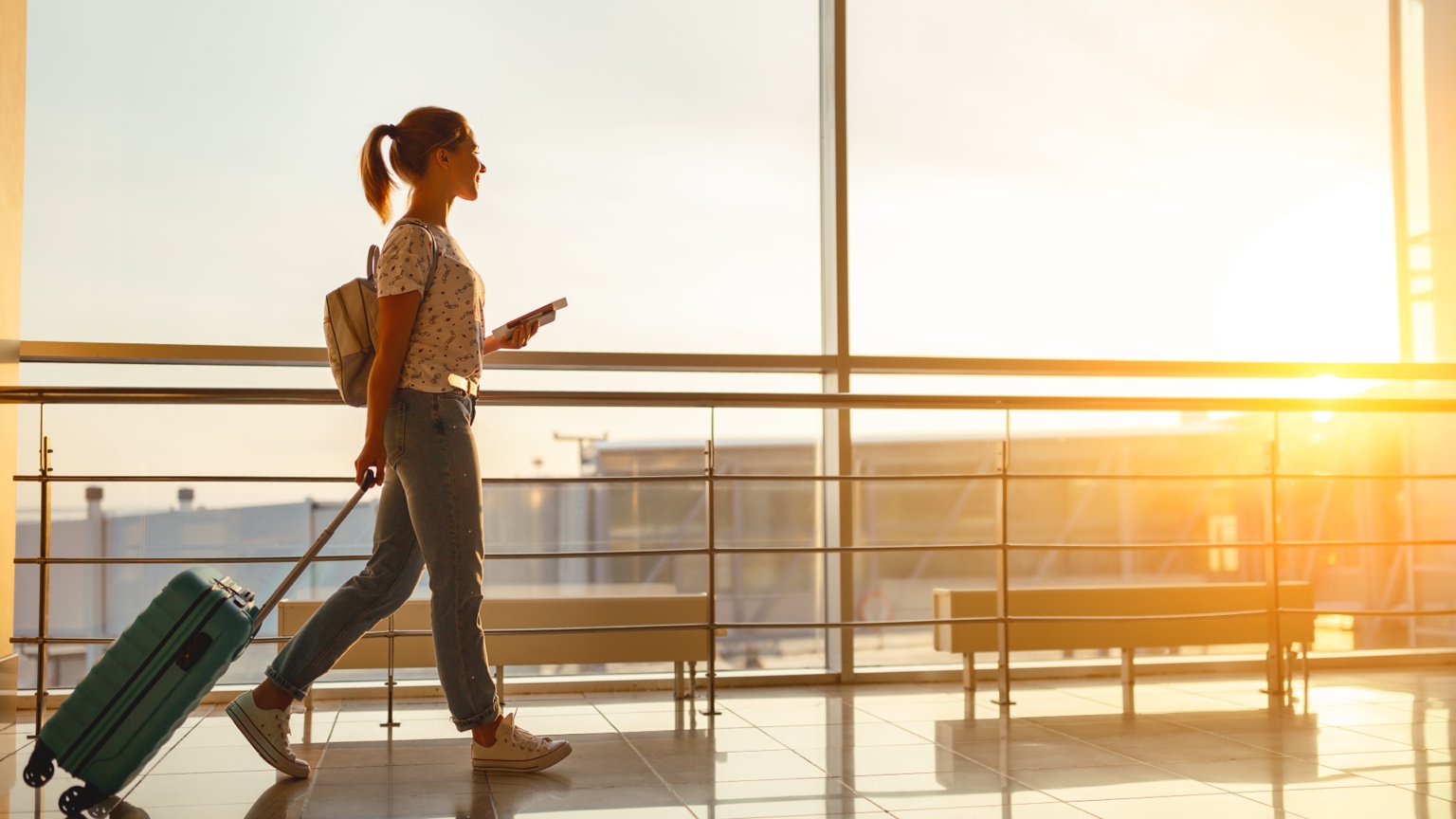Traveler pulling a suitcase through an airport terminal at sunset