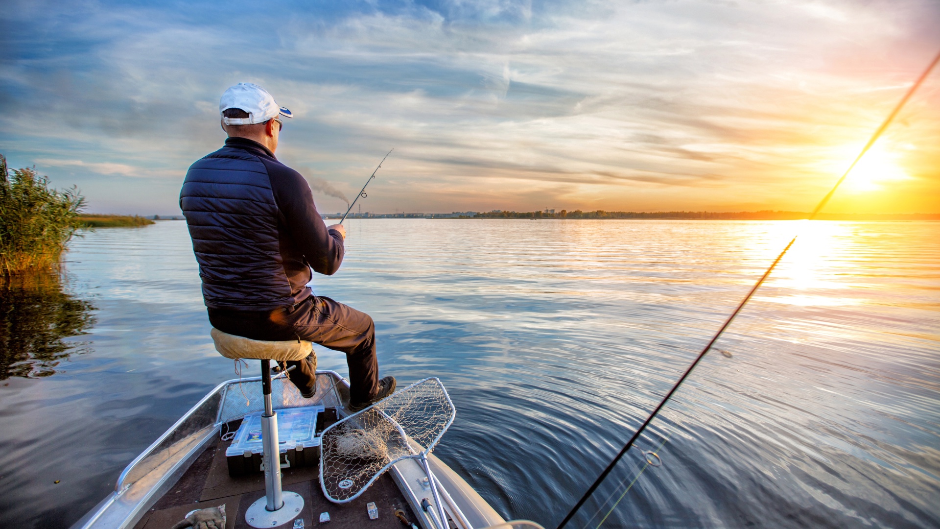 Person fishing from a boat at sunset