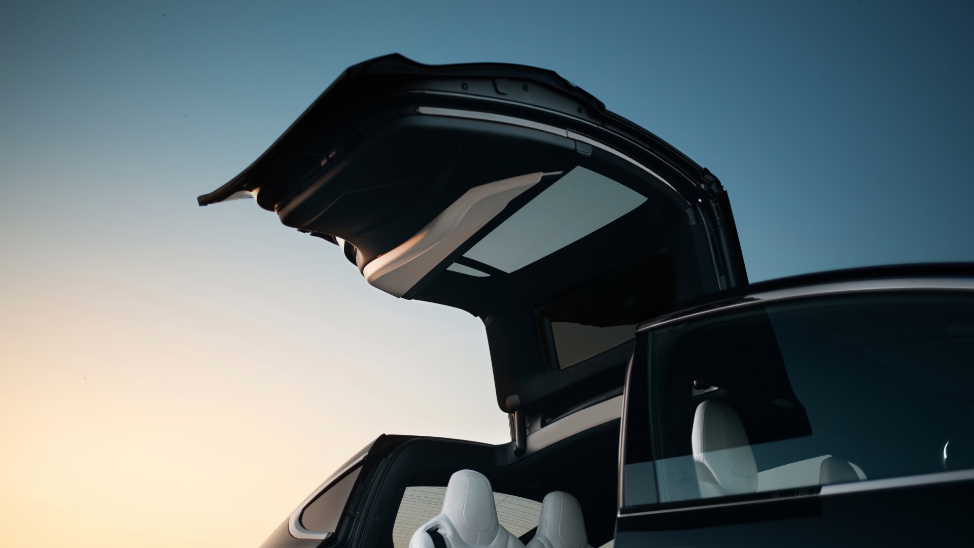 Tesla Model X with a falcon-wing door raised at sunset