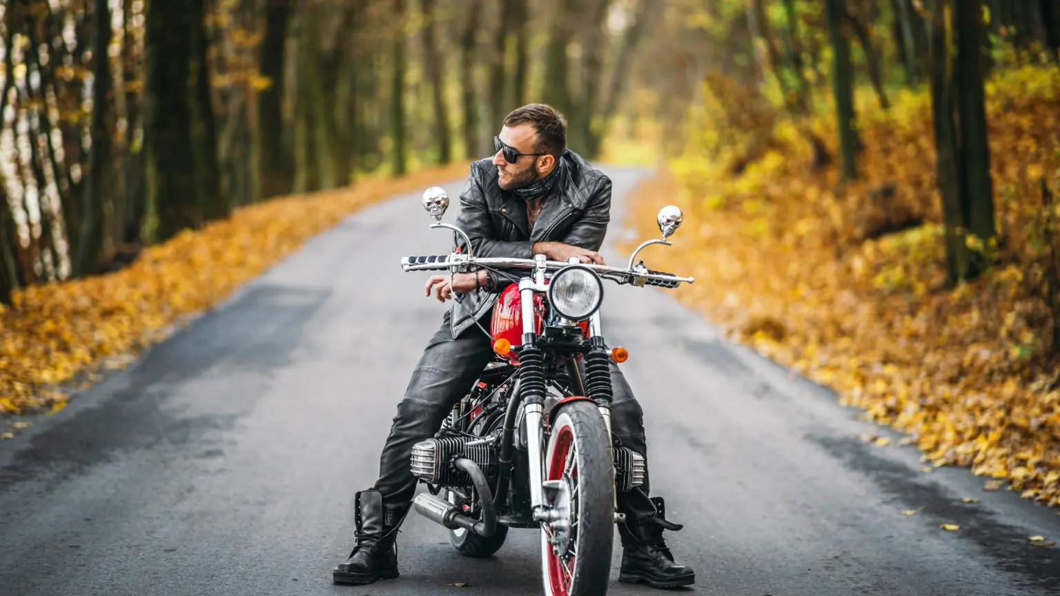 Rider seated on a red motorcycle along a tree-lined road