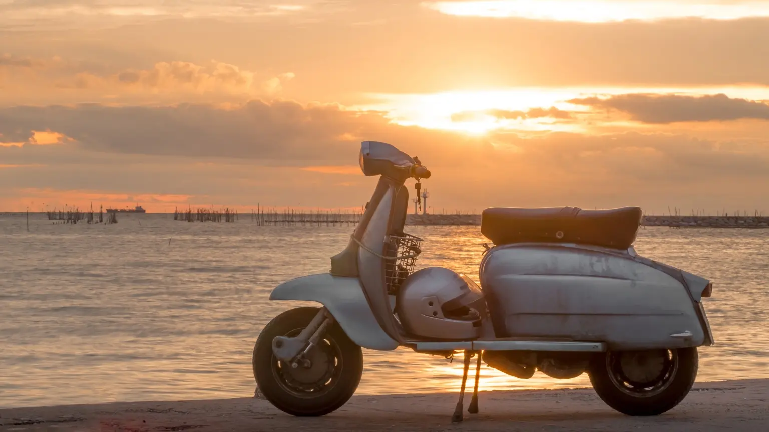 Vintage scooter parked beside the water at sunset