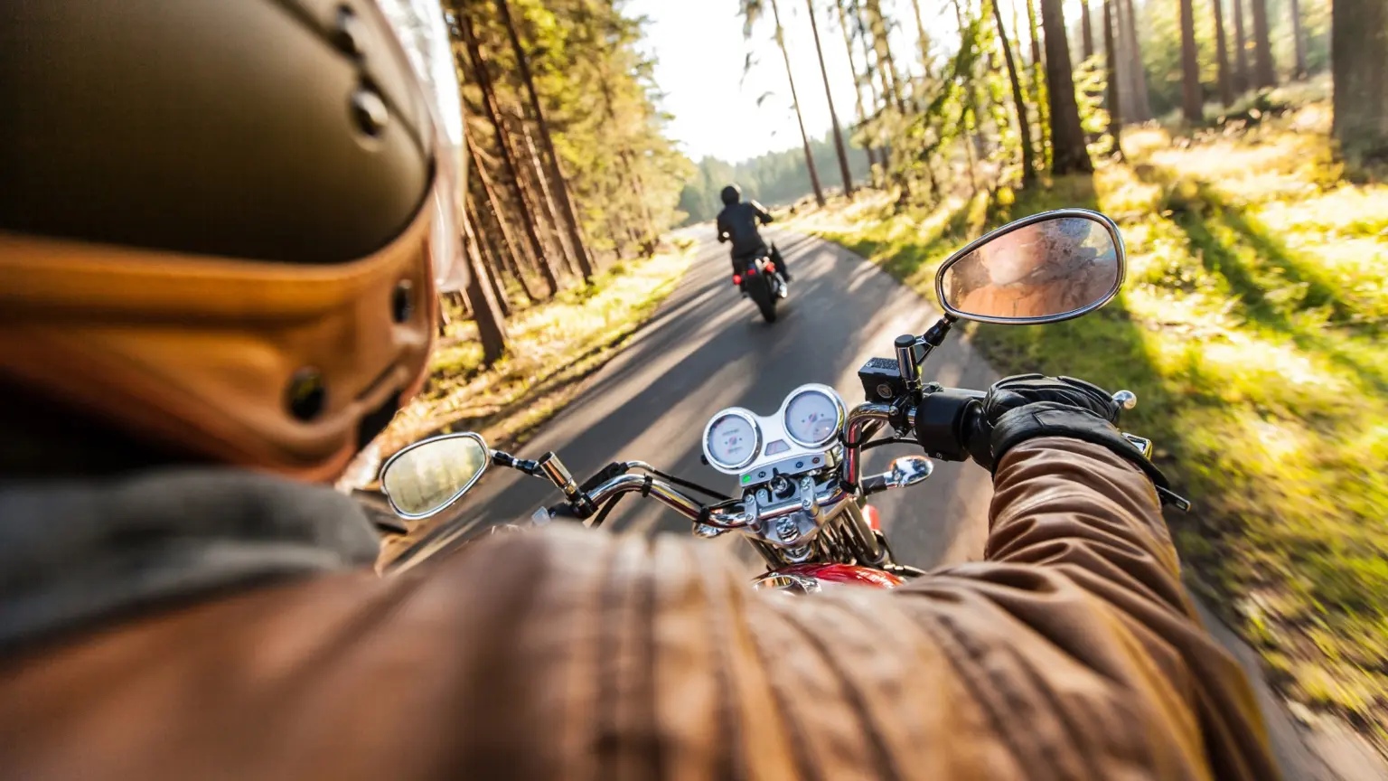 Motorcyclist riding with a companion along a forest road