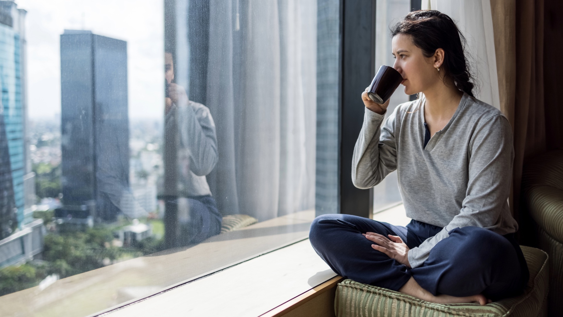 Woman enjoying a drink beside a city apartment window