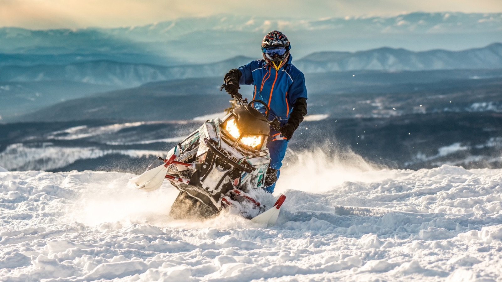 A snowmobiler riding across a mountain trail