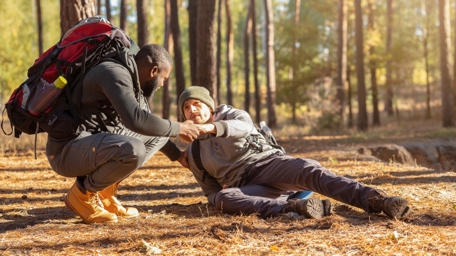 Hiker helping another hiker seated on a forest trail
