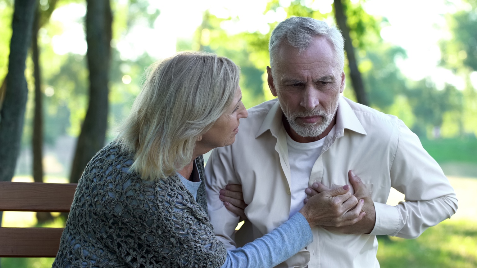 Woman supporting a man holding his chest on a park bench