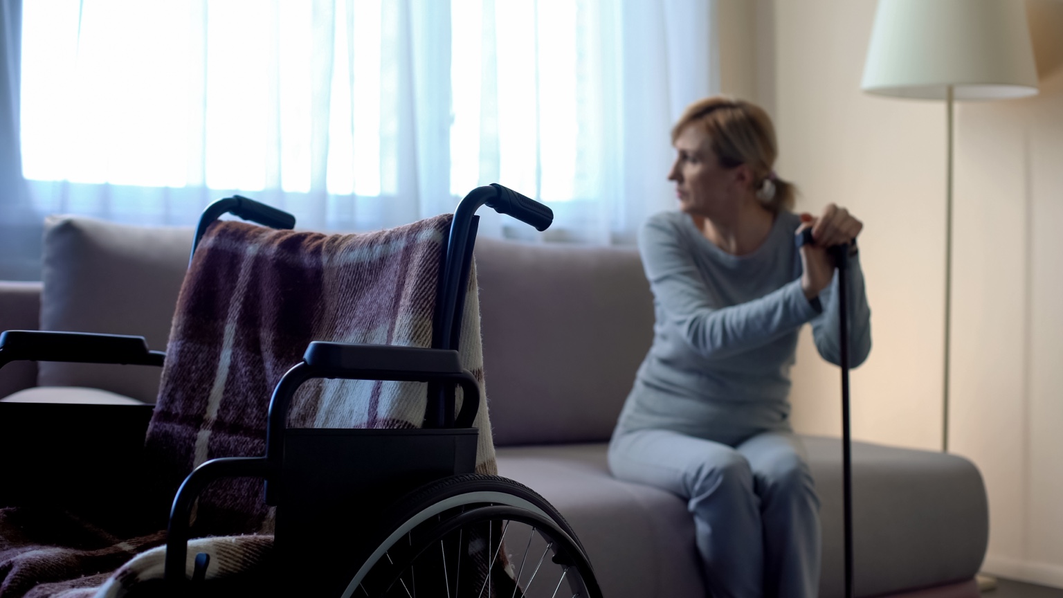 Woman seated with a cane beside a wheelchair at home