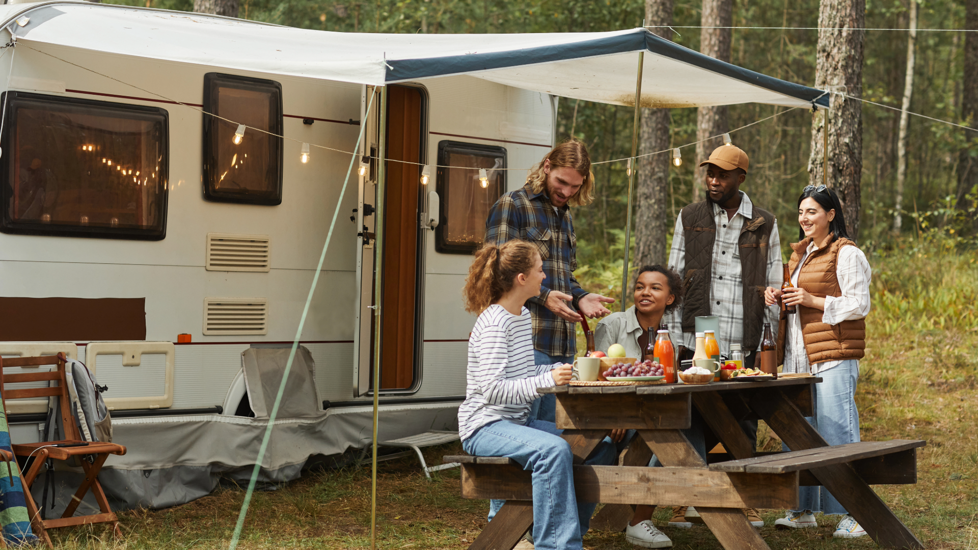 Five friends sharing a picnic beside a travel trailer