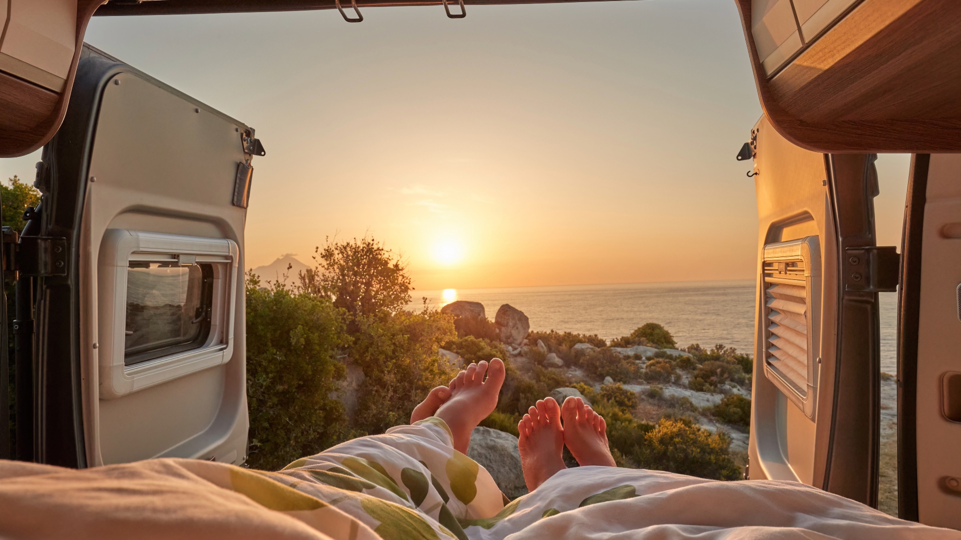 Coastal sunset viewed through the open doors of a camper van