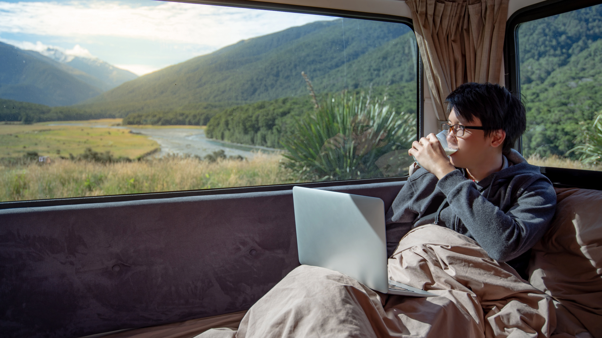 Traveler with a laptop enjoying a mountain view from inside a travel trailer